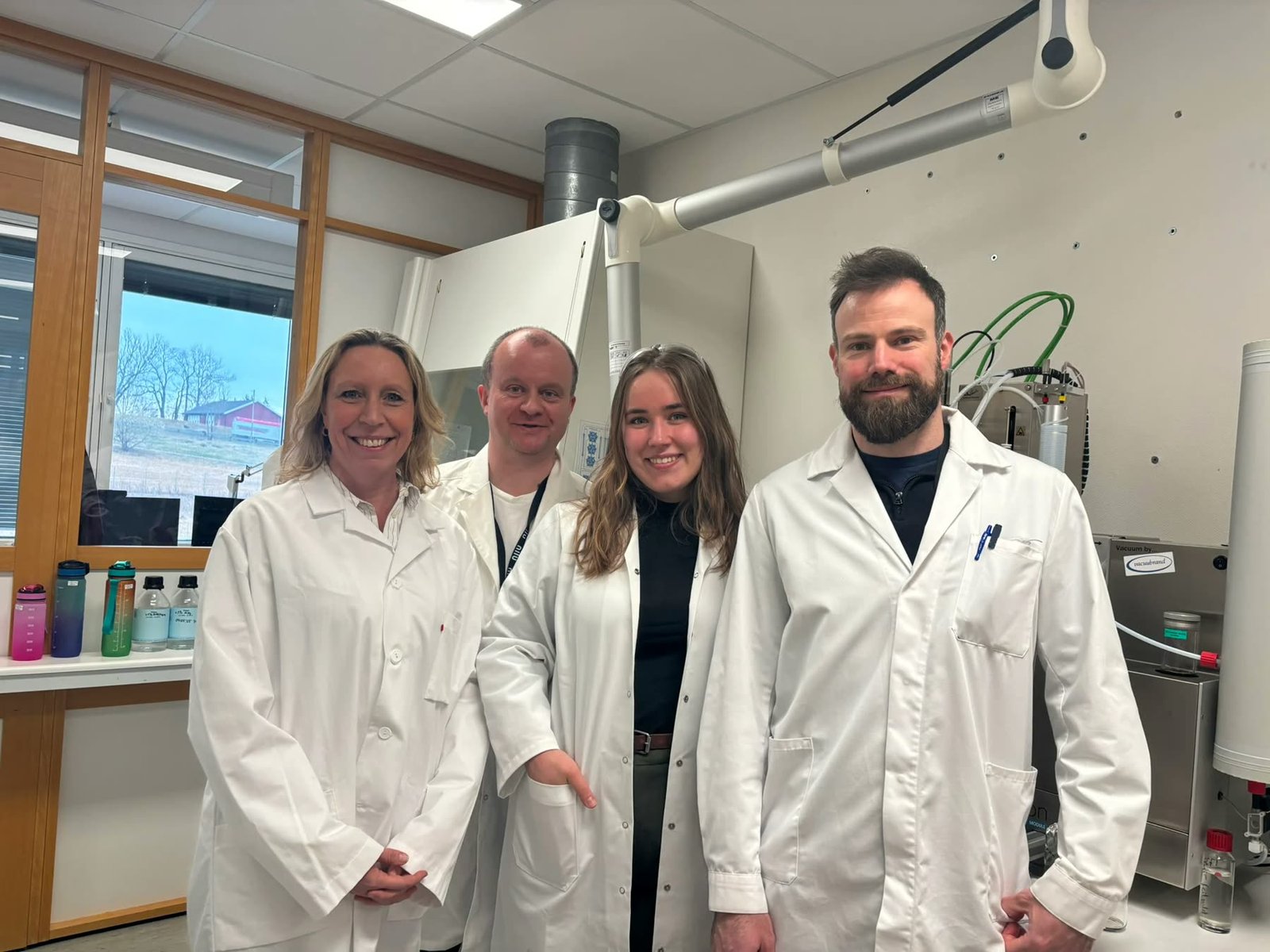 Fire ansatte i hvite laboratoriefrakker smiler i laboratoriet